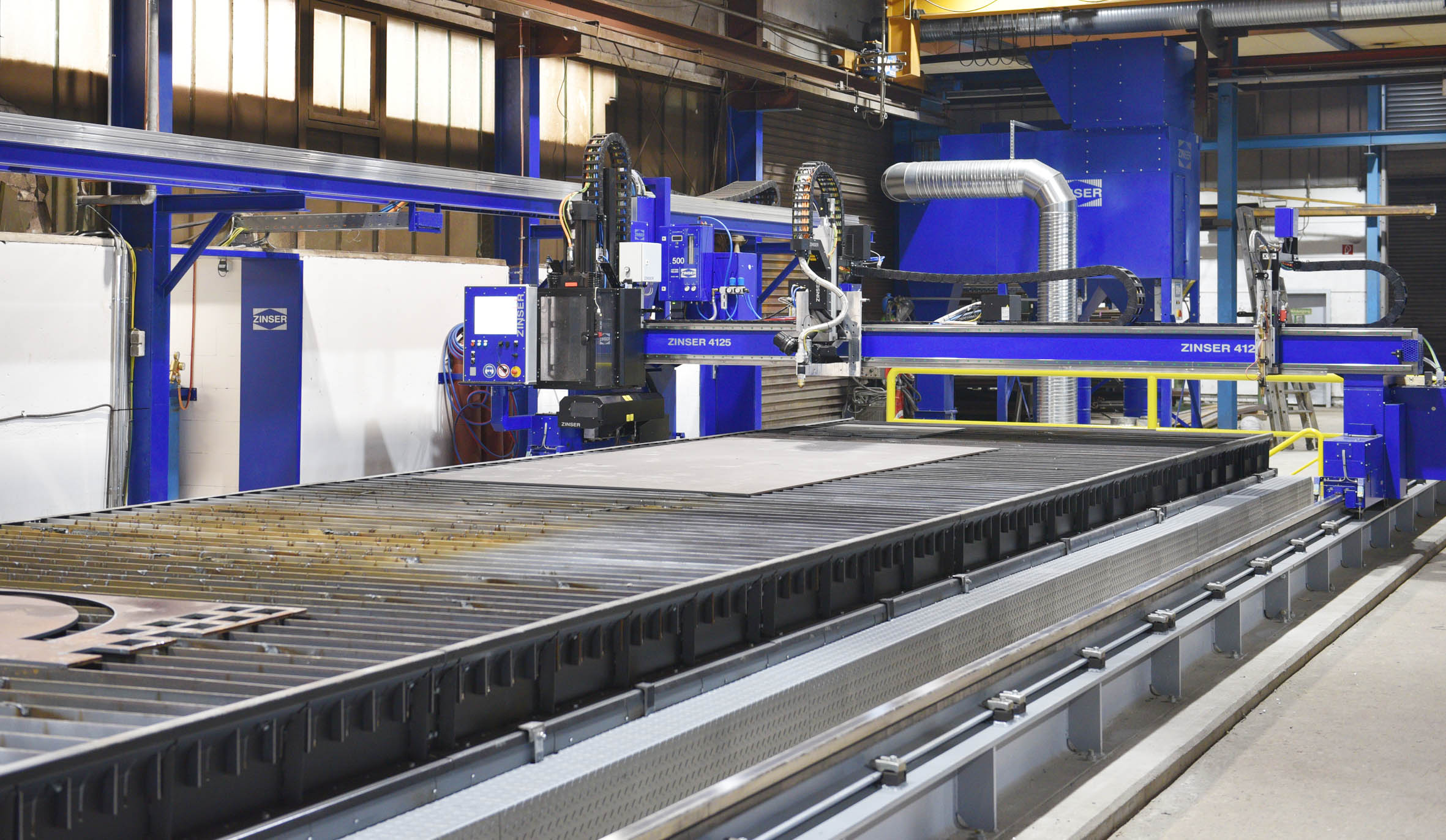 ZINSER 4125 CNC Schneidmaschine mit Autogenbrenner, Plasmabrenner und Bohreinheit über einem ZINtrac Schwingfördertisch.