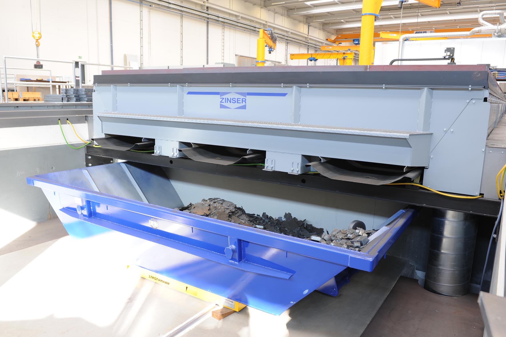 Rear view of a ZINtrac vibrating conveyor table embedded in the floor. The burning residues and cutting slags generated during the plasma or oxy-fuel cutting operation are transported by the vibrating conveyor troughs out of the table system and into the provided receptacles.